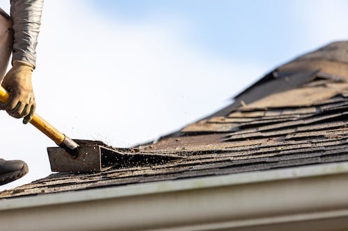 A roofing contractor removing roof shingles and needing to dump them near him