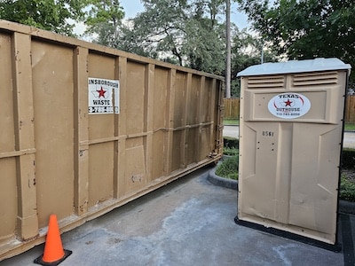 Gainsborough Waste roll-off dumpster next to a Texas Outhouse portable toilet at a job site in Houston, TX